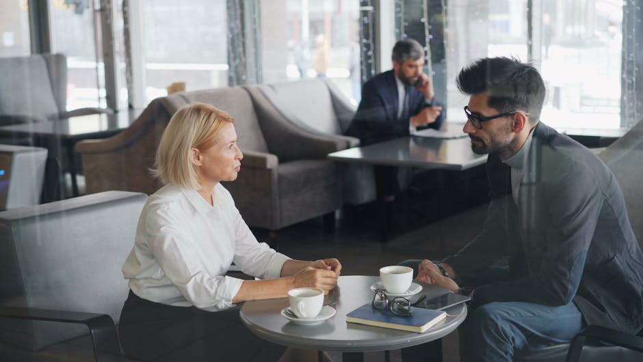 Two coworkers having a business meeting in a cozy café, discussing over coffee.